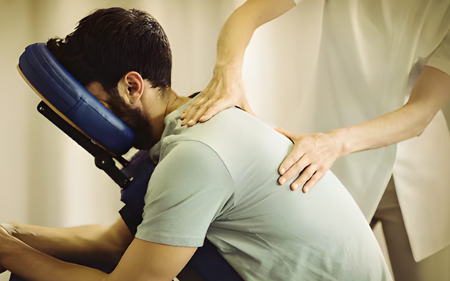 A massage therapist working on the back and shoulders of a man relaxing in a massage chair