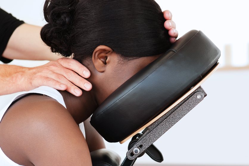 A woman resting in a massage chair while a therapist massages her neck